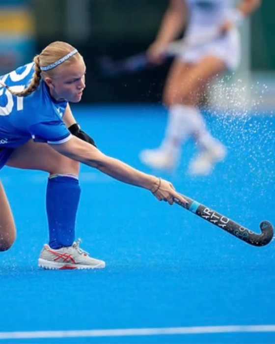 Darcy Littlefield reaching to control the ball on a blue hockey pitch.
