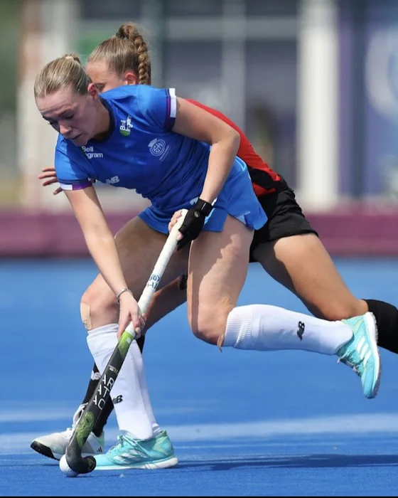 Katie Brett carrying the ball during a competitive hockey match.